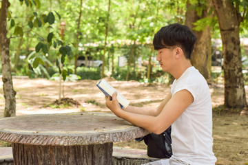 Feeling tired. Young man holding book sitting on bench in the park and keeping eyes closed