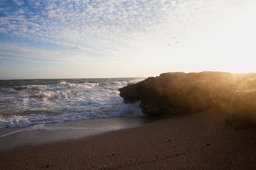 Beautiful colorful dawn over sea and waves hitting and splashing rocky stone beach