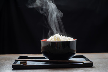 Cooked rice with steam in black bowl on dark background,hot cooked rice in bowl selective focus,hot...