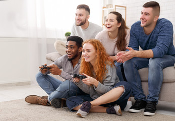 Diverse friends playing video games, sitting on floor at home