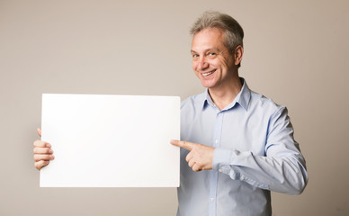 Mature man holding blank board and pointing on it