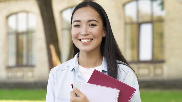Close up portrait of pretty smiling student girl holding textbooks. Looking aside and then at the camera.