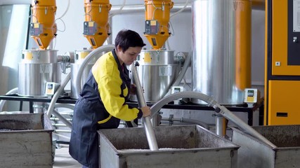 Production plant worker Works with loader Hose vacuum sucking white virgin plastic granules from tank in factory workshop