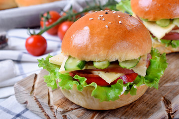 Sandwich with ham, cucumbers, tomatoes, lettuce leaves and cheese on wooden board