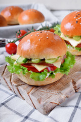Sandwich with ham, cucumbers, tomatoes, lettuce leaves and cheese on wooden board