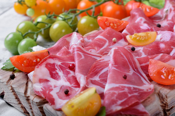 Thin slices of Italian cold cut pork Coppa and cut cherry tomatoes on wooden board