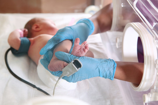 Three-day-old newborn baby in intensive care unit in a medical incubator. Macro photo of doctor's hands and legs of a child. Newborn rescue concept. The work of resuscitation doctors.