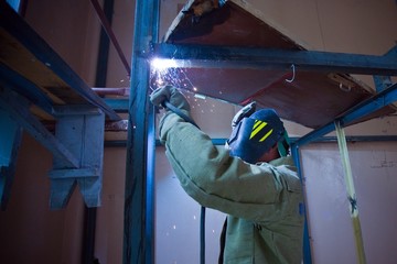Welder in mask welding metal construction on open air.