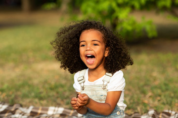 Laughing little girl sitting on blanket on grass, resting outdoors