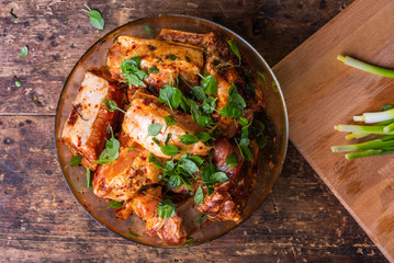 Slices of pork with ribs marinated in spicy sauce with basil in a glass bowl close-up