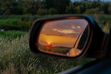 A golden sunset seen in an outside rear view car mirror