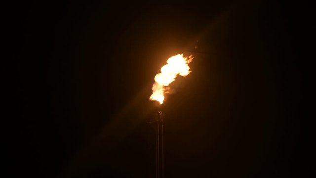 A night shot of a flaming gas torch of petrochemical production in complete darkness. Low key oil combustion and environmental pollution. Ecology problems concept