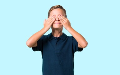 Little boy covering eyes by hands on blue background
