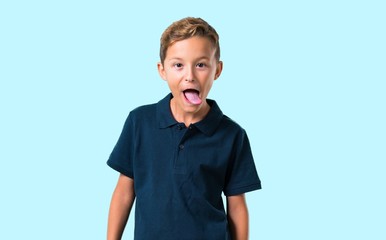 Little boy showing tongue at the camera having funny look on blue background