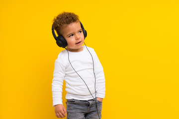 kid over isolated yellow background listening music