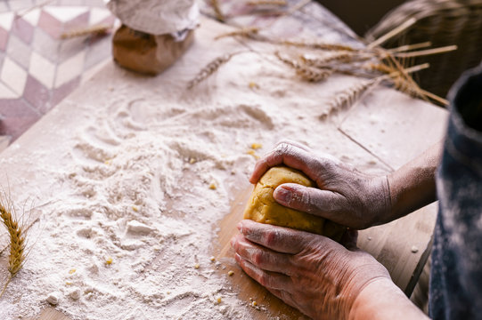 Female hands and dough. A woman is preparing a dough for home baking. Rustic style photo. Wooden table, wheat ears and flour. Free space for text.