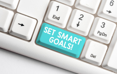 Conceptual hand writing showing Set Smart Goals. Concept meaning list to clarify your ideas focus efforts use time wisely White pc keyboard with note paper above the white background