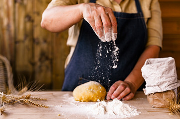 Women's hands, flour and dough. Levitation in a frame of dough and flour. A woman in an apron is preparing dough for home baking. Rustic style photo. Wooden table, wheat ears and flou.Emotional photo