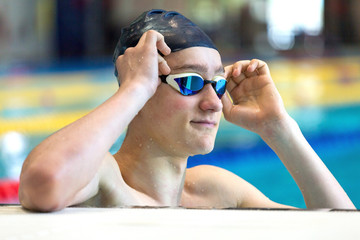 A teenage athlete improves swimming goggles in an indoor pool. Close up, selective focus.