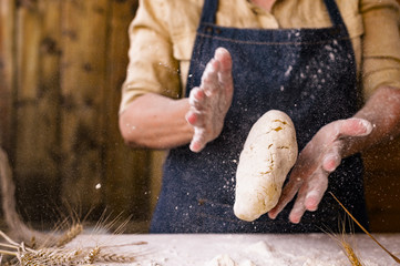 Women's hands, flour and dough. Levitation in the frame. A woman in an apron is preparing dough for home baking. Rustic style photo. Wooden table, wheat ears and flour in the crucifix. Emotional photo