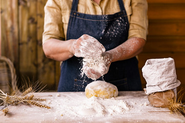 Female hands and dough. A woman is preparing a dough for home baking. Rustic style photo. Wooden table, wheat ears and flour. Free space for text
