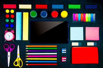 Colorful office supplies neatly geometrically evenly laid out on blackboard background. Pencils, scissors, sharpeners, plasticine, alarm clock, tablet on canvas. Preparing perfectionist for study.