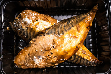 cooked headless mackerel in a black plastic container