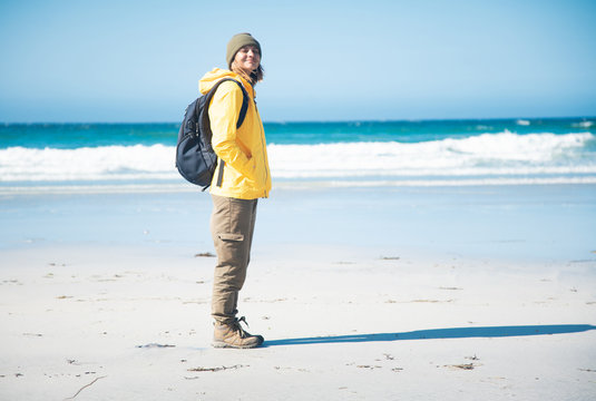 Happy girl traveler in a yellow jacket and hat on the beach on the Lofoten Islands, travel Norway, Northern Europe