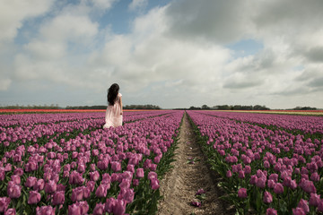 girl in pink dress running  in colorful purple field of tulip flowers 