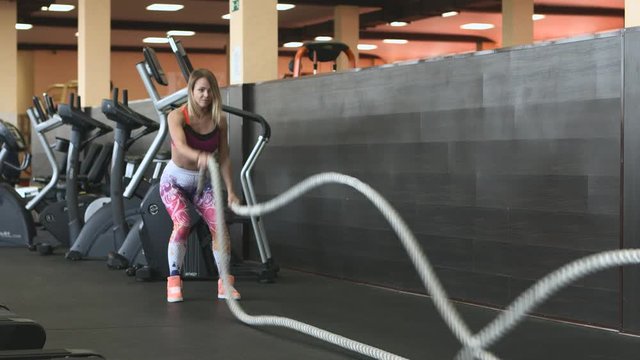 An attractive young and athletic girl using training ropes in a gym.