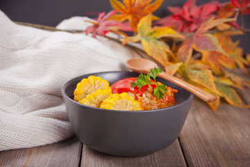 Stuffed peppers with minced meat, rice and corn in the bowl on the wooden table. Autumn hot food