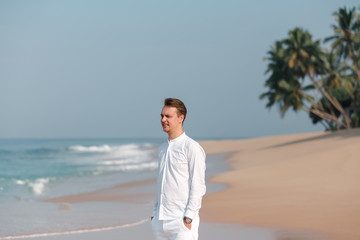 Handsome man wearing white clothes posing in sea scenery. Handsome happy man wearing white shirt at the sea or the ocean background. Travel vacation holiday. Man walking at the sea
