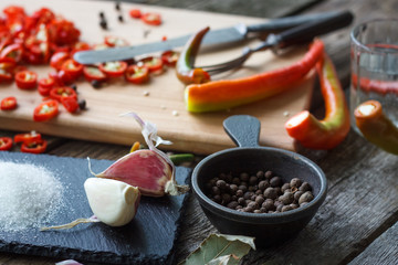 Close-up of chopped hot chili peppers and heaps of salt, sugar, garlic, allspice, bay leaf on an old wooden surface, selective focus