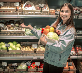 Fototapeta premium Young girl holding fruits and vegetables in an eco bag on the background of the store