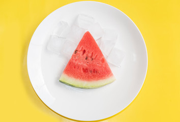 Slice watermelon with ice on a white plate and on a yellow background.