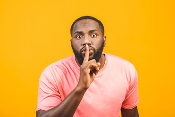 Just don't speak! Close up portrait of handsome cheerful mysterious afro american silent man making hush gesture, isolated on yellow background.