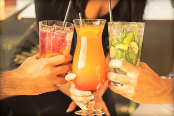Hands with tropical cocktails at  party. Young people drinking cocktails, summer vacation concept.  Focus on bottom hands glass - Image