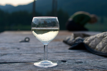 one glass of white wine and a jacket on evening on a wooden foodbridge in background 