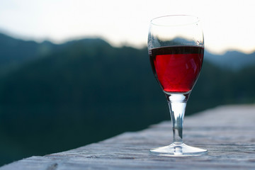 ein glas rotwein auf holzsteg in abendstimmung am spitzingsee bayern mit bergsilhouette