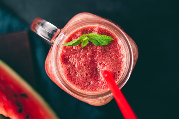Watermelon red smoothie in jar with fresh mint leaves on dark background, top view