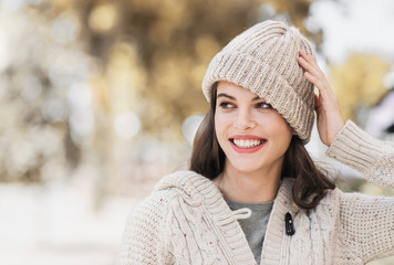 Beautiful happy woman autumn portrait. Smiling girl wearing warm clothes and hat in a city in winter