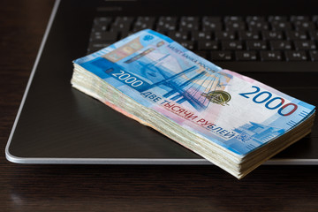 Earnings on the Internet concept. Stack of russian rubles lay on laptop keyboard.