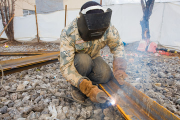 Welder in mask welding metal construction on open air.