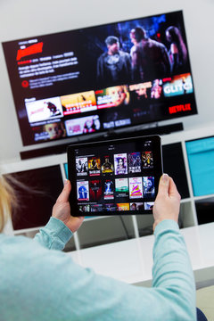 Woman Holding a touch pad and switching channels on France Netflix HomePage. with TV set on background.