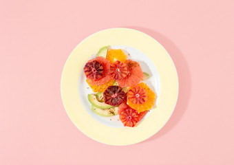 Summer fruit vitamin salad of grapefruit, orange and avocado on a pink background top view flat lay
