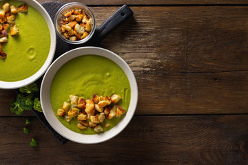 Bowl of cream broccoli soup with bread croutons on a wooden background