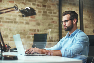 Young freelancer. Side view of handsome bearded businessman in eyeglasses and formal wear working...