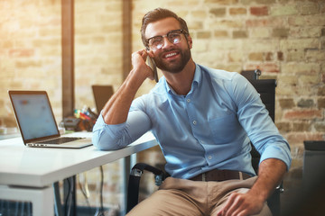 Great news Portrait of young bearded businessman in eyeglasses and formal wear talking on the phone...