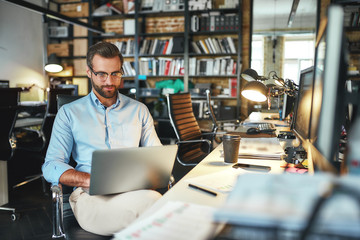 Comfortable workplace. Portrait of young and successful bearded man in eyeglasses working with...