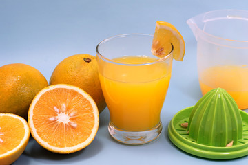 a glass of sweet orange juice with orange slices and squeezer isolated on blue